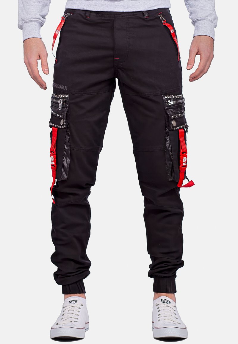 Schwarze Cargo-Hosen mit roten Akzenten, mehreren Taschen, Reißverschlussdetails und Nietenverzierungen. Umschläge an den Knöcheln und strapazierfähiger Stoff.