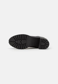 Black rubber shoe sole with a textured tread pattern, featuring deep grooves for grip and stability, designed for durability and traction.