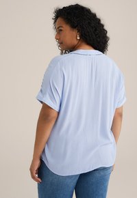 Top de manga corta azul claro con una textura suave, que presenta un escote redondo y detalles de costura sutiles en la parte posterior. Combinado con jeans.