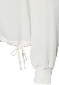 Nahaufnahme des Ärmels eines weißen Sweatshirts mit geripptem Bündchen und Saum, der eine verstellbare Kordel hat, die zu einer Schleife gebunden ist.