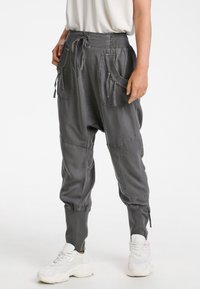 Grå harempants har en hög elastisk midja, snörningsstängning och två stora framfickor med en avslappnad passform och avsmalnande muddar.