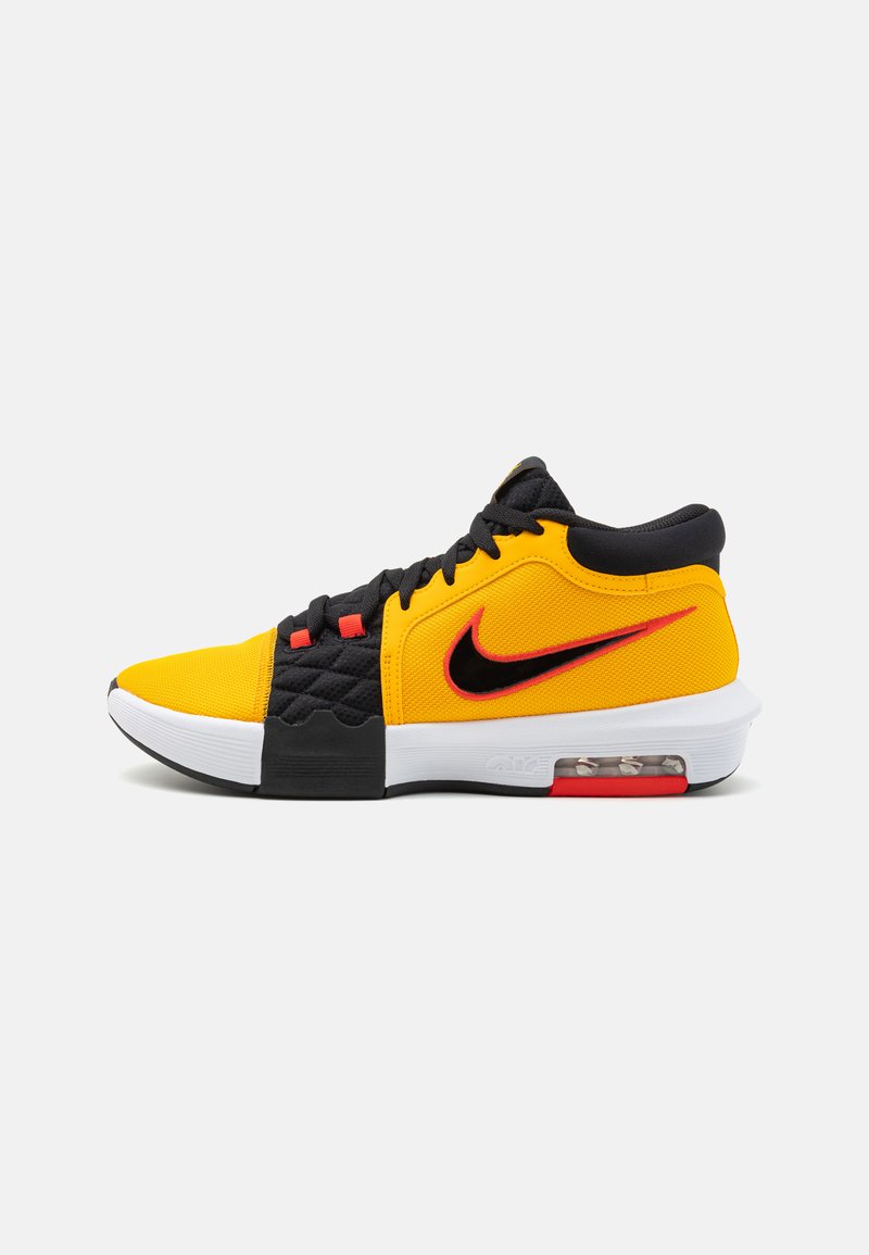 Nike-sko med en blanding af gult stof, sorte accenter og en hvid sål med en synlig luftenhed; rød brandingdetalje.