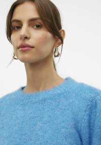 Maglione blu a maglia con una finitura tessurizzata e fuzzy e un collo rotondo. Gli orecchini a cerchio astratti in oro in evidenza completano l'outfit.