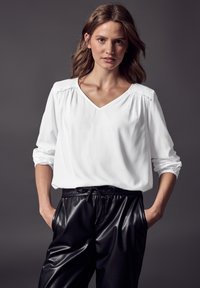 Witte blouse met lange mouwen, een V-hals en geplooide details op de schouders, gecombineerd met zwarte leren broek met een tailleband met trekkoord.