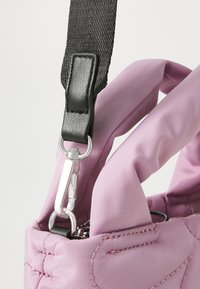 Geantă din material roz, cu o suprafață texturată, curea neagră, accesorii din metal argintiu și un cârlig de tip carabină pentru versatilitate.