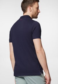 Granatowa koszulka polo z klasycznym kołnierzykiem, krótkimi rękawami i bocznymi rozcięciami, wykonana z teksturowanej bawełny. Delikatne logo na plecach.