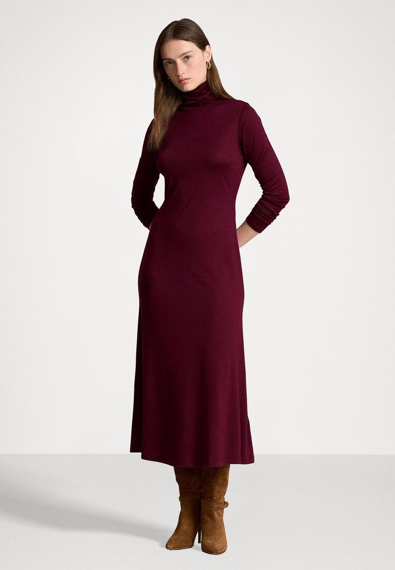 Burgunderfarbene Rollkragenkleid mit langen Ärmeln, taillierter Passform und ausgestelltem Saum, kombiniert mit braunen kniehohen Stiefeln. Weiche Strickstruktur.