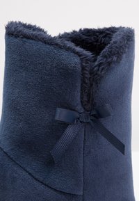 Chausson bottine en tissu doux bleu foncé avec doublure fourrure et petit nœud décoratif sur le côté près de l'ouverture de la cheville.