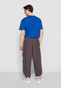 T-shirt bleu en coton pour homme associé à un pantalon cargo noir lose avec des poches latérales. Stylé avec des baskets blanches.