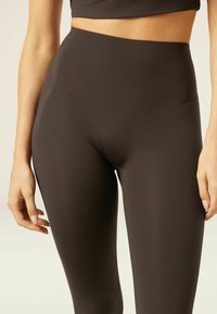 Leggings taille haute de couleur marron foncé en tissu lisse et extensible. Présentent un design sans couture et s'ajustent parfaitement à la taille et aux jambes.