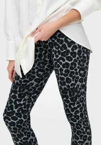 Svart och grå leopardmönstrade leggings tillverkade av ett elastiskt tyg, med en tight passform och en mjuk yta.