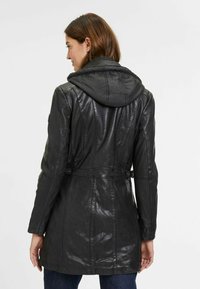 Giubbotto di pelle nera con cappuccio trapuntato e removibile, vita con cintura e cuciture strutturate. Design semplice, texture liscia, silhouette elegante.