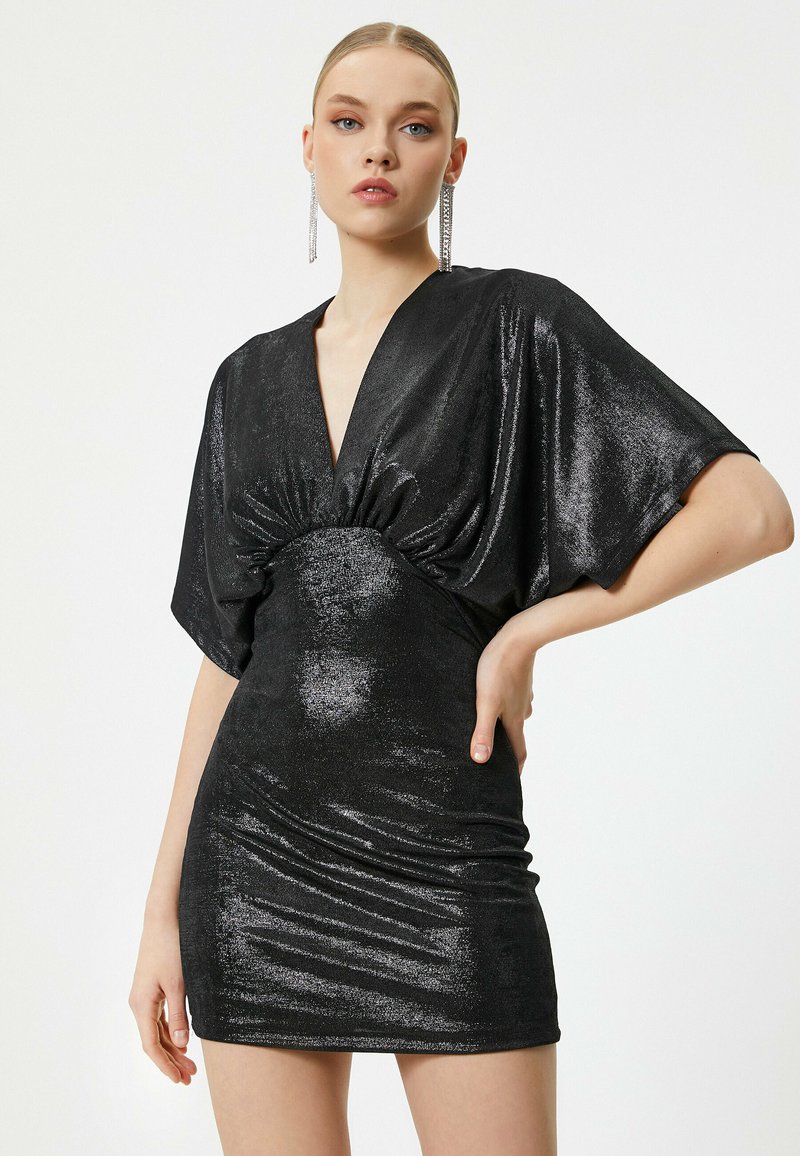 Zwarte glanzende jurk met een diepe V-hals, korte mouwen en geraffineerde details bij de taille. De gladde textuur accentueert de silhoutte.