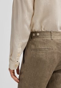 Beige linnen skjorta med knäppta manschetter, i kombination med bruna texturerade byxor med sidofickor och en bakficka med passpoal.