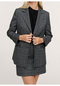 Blazer grigio a quadri con una vestibilità strutturata, rever affilati, bottoni doppi e maniche lunghe, abbinato a una gonna coordinata.