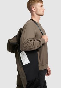 Černý batoh s matným povrchem, který má velkou hlavní přihrádku, nastavitelná ramenní popruhy a božní štítek s pokyny k údržbě.