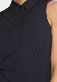 Polo senza maniche di colore blu navy realizzato in un tessuto liscio, con colletto e un placket con bottoni a scomparsa, caratterizzato da un piccolo logo sul petto.