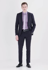 Marineblauer Anzug in maßgeschneiderter Passform, kombiniert mit einem helllila Hemd und Krawatte; schwarze Schuhe betonen den eleganten Look.