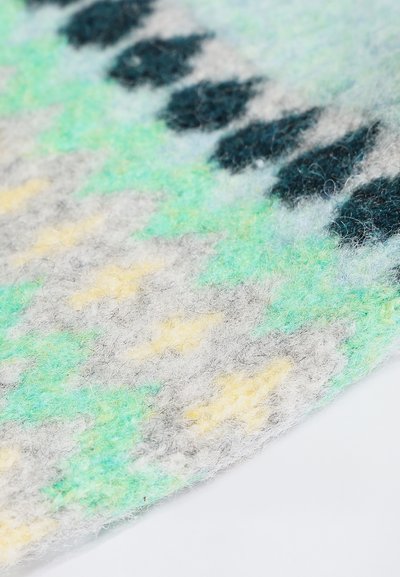 Μαλακό πλεκτό ύφασμα με χνουδή υφή που παρουσιάζει ένα μοτίβο από μαύρα, πράσινα, κίτρινα και γκρι γεωμετρικά σχήματα σε λευκό φόντο.