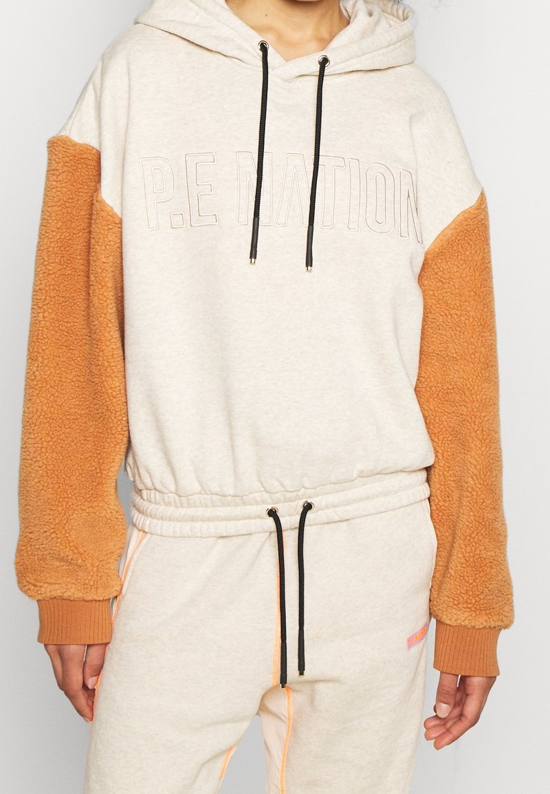Felpa con cappuccio di colore beige con maniche in pile arancioni. Presenta polsini a coste, chiusura con coulisse e logo stampato sulla parte frontale.