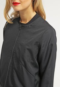 Czarna katana bomberka wykonana z gładkiego, lekkiego materiału. Posiada zamek błyskawiczny, prążkowany kołnierz oraz boczne kieszenie.