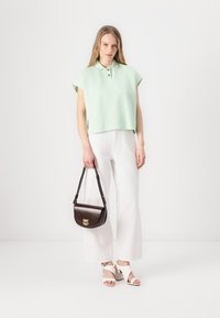 Mintgroene cropped poloshirt met gouden knopen, gecombineerd met witte wijde broek en witte hakken. Bruine schoudertas met een haaksluiting.