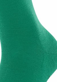 Primo piano di un piede che indossa una calza verde uniforme con una texture a coste e un'area del tallone rinforzata.