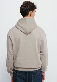 Kapuzensweatshirt in einem hellbeigen Farbton, mit einer weichen Textur und gerippten Bündchen. Die Rückseite zeigt ein klares Design ohne Verzierungen.