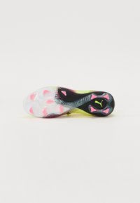 Botas de fútbol con suela translúcida, acentos en negro y detalles en rosa. Presenta un patrón de agarre texturizado y logo en el talón.