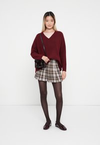 Bordeaux v-hals trui, geruite minirok in beige en bruin, zwarte panty's en bordeaux balletflats. Zwarte crossbody tas met zilveren hardware.