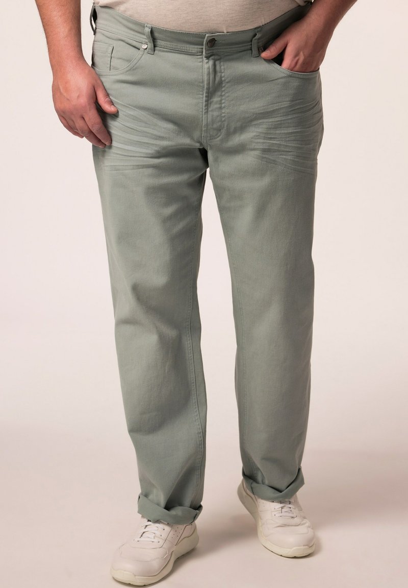 Vihreät puuvillahousut, joissa on sileä pinta, viisi taskua ja käännetyt lahkeet, yhdistetty valkoisiin lenkkitossuihin.