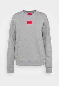 Sudadera gris con cuello redondo, que presenta un parche de logo rectangular rojo etiquetado como "HUGO". Textura suave, corte relajado, puños y dobladillo acanalados.