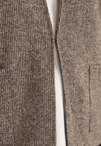 Brun ribbad cardigan med en texturerad väv. Har en öppen front, två sidfickor och ett mjukt foder som syns under.