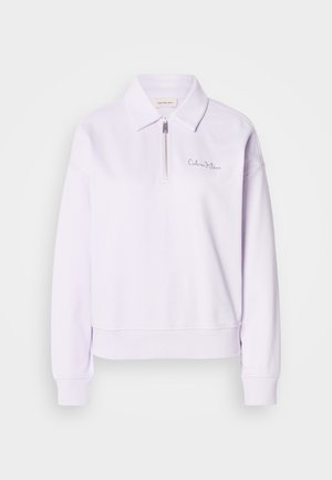 Lys lilla genser med krage og halv glidelås. Har ribbestrikkede mansjetter og kant, med subtil logo-brodering på brystet.