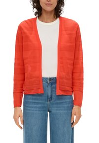 Cardigan rouge en tricot avec des rayures horizontales, ouverture sur le devant et manches longues, associé à un haut blanc et un jean bleu taille haute.
