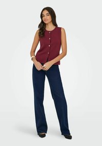 Burgundia ilma varrukatega pluus hõbedaste nööpidega, koos tumesiniste laiade pükste paariga. Sile kangas, struktureeritud disain sobitatud silueti jaotusega.