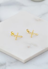 Orecchini a forma di croce in oro, decorati con strass trasparenti, con una finitura lucida e chiusure a farfallina, su una superficie di marmo chiaro.