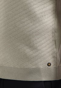 Gebreid pullover in lichtgrijs met een gestructureerd ruitpatroon, geribde zoom en een klein hexagonaal embleem aan de onderzijde.