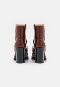 Bottes basses en cuir marron brillant avec un col contrastant couleur camel, bouts carrés et talons noirs épais. Disposent d'une fermeture éclair latérale pour un accès facile.