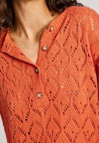 Stickad orange cardigan med diamanter, V-ringning och tre bruna knappstängningar fram. Texturerad yta hela vägen igenom.