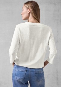 Weißes Langarmoberteil mit lockerer Passform, Rundhalsausschnitt und weicher Textur, kombiniert mit mittelblauen Denim-Jeans.
