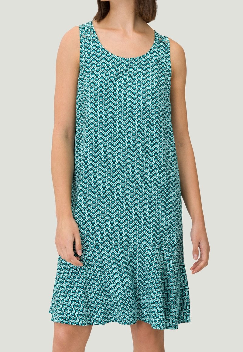 En ærmeløs kjole i teal med et geometrisk mønster af sammenflettede cirkler, med en udvidet kant og glat tekstur.