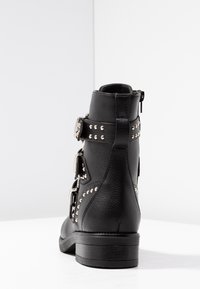Stivali neri alla caviglia con finitura in pelle texturizzata, dotati di borchie e fibbie in argento, tacco basso e zip laterale per la chiusura.