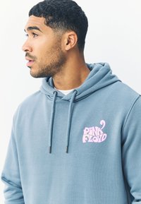 Šviesiai mėlynas džemperis su raišteliais, minkšta tekstūra. Ant kairės krūtinės pusės yra rožinė "PINK FLOYD" logotipas. Paprastas dizainas su laisvu siluetu.