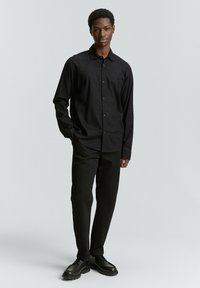 Zwarte langemouwen shirt met knopen, gecombineerd met zwarte broek en schoenen. Soepele stof textuur, klassieke ontwerp met een ontspannen pasvorm.