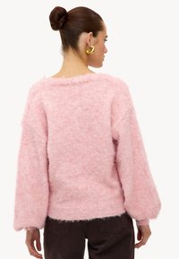 Pull rose duveteux à coupe ample, manches larges et ourlet côtelé. Texture douce et apparence légèrement transparente. Vue de dos présentée.