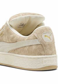 Vaj színű szuede sneaker fehér díszcsíkkal és krém színű belső résszel. Texturált gumitalppal és arany logós részlettel a sarkán.