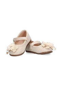 Zapatos de tela tejidos color beige con punta redondeada, correa ajustable y adornos de flores color crema en la parte delantera. Suela plana de goma marrón.