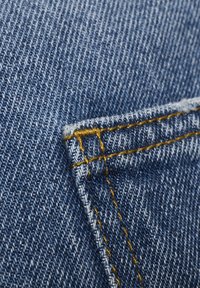 Lähedal olev sinine teksariie, kus on näha tasku nurka oranži õmblusega.