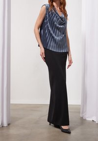 Námořnický bezrukávový top s drapovaným výstřihem a vertikálními sklady, spárovaný s dlouhou černou sukní a černými špičatými podpatky. Hladké textury.